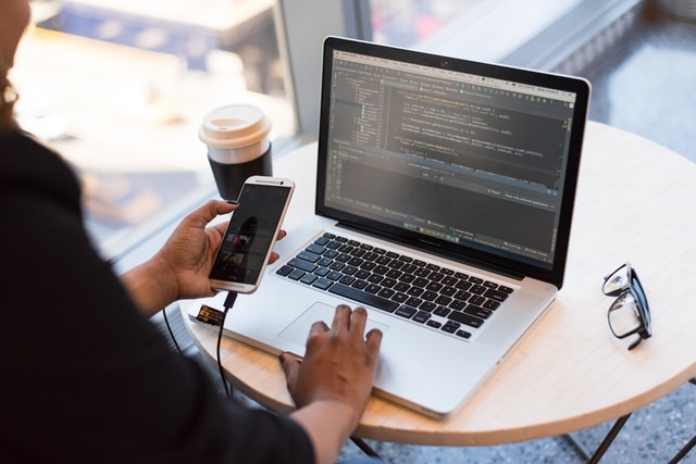 person-holding-smartphone-while-using-laptop