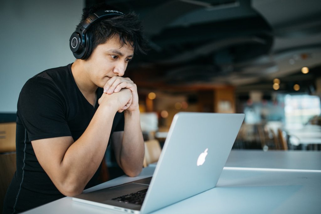 man-sitting-wearing-headphones-facing-laptop